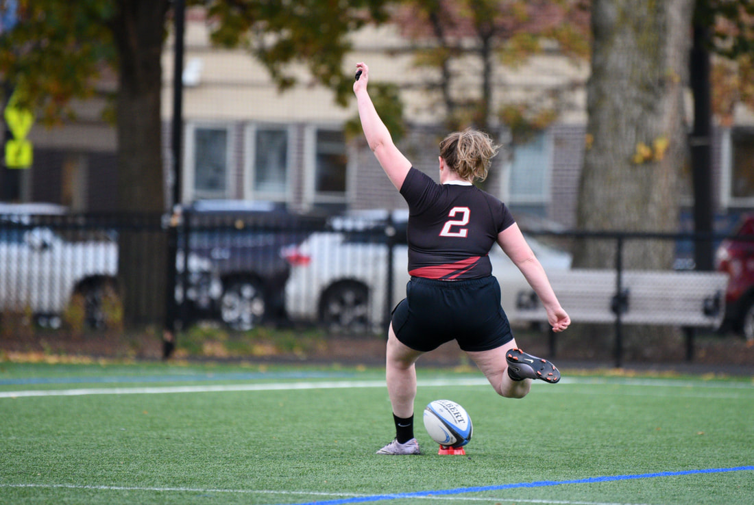 Rugby player kicking ball on turf. Player wears a black uniform with the number two on the back.